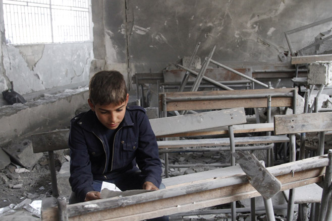 A Syrian boy sitting in his destroyed sc
